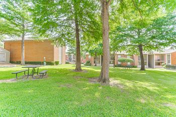 A grassy area with trees and a picnic table in front of a building.
